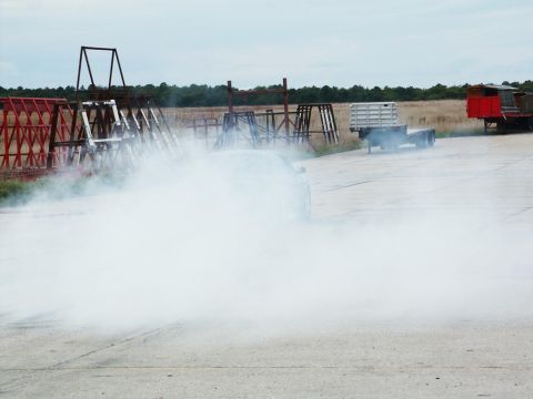 2001 Mercury Grand Marquis - A car performs a burnout, generating a large cloud of smoke, with two trucks visible in the distance.