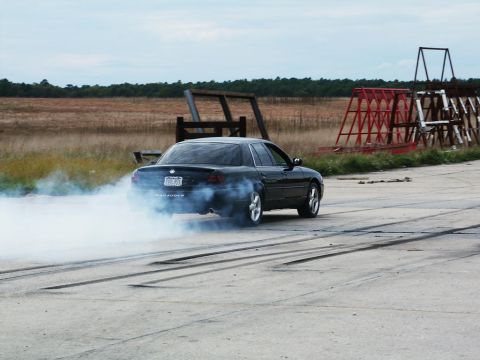 2001 Mercury Grand Marquis - A black sedan performs a burnout, leaving a trail of smoke on the asphalt. The word 'Marauder' is visible on the rear of the vehicle.