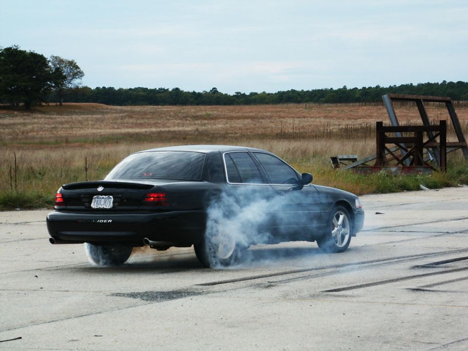 Black sedan doing a burnout, kicking up smoke. License plate visible