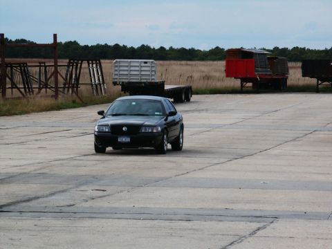 2001 Mercury Grand Marquis - A black 2001 Mercury Grand Marquis sedan is seen from the front on a concrete surface with trailers in the background.