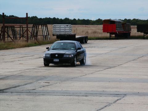2001 Mercury Grand Marquis - A black 2001 Mercury Grand Marquis performs a burnout on a concrete surface with trailers in the background.