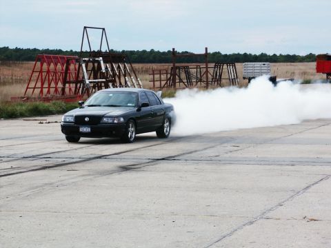 2001 Mercury Grand Marquis - A black sedan performs a burnout on a paved surface, kicking up a large cloud of smoke.