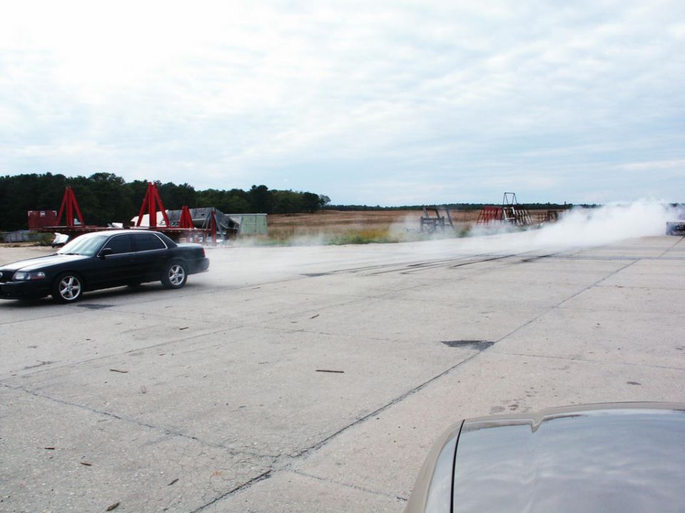 Black 2001 Mercury Grand Marquis doing a burnout on a concrete track