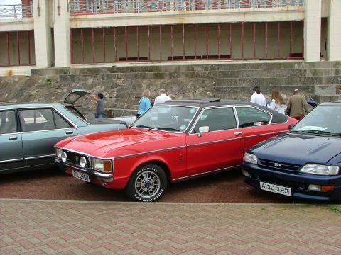2001 Ford Fiesta - A red coupe and a blue hatchback are parked side-by-side near a waterfront promenade.