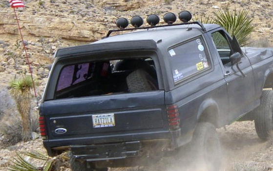 Rear of dark blue Ford Bronco with RATZILA plate and roof light bar on rocky trail