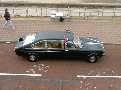 2001 Ford Fiesta - A black sedan decorated with Union Jack flags and white ribbons is parked by the promenade.