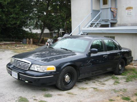 1999 Ford Crown Victoria - A dark blue sedan is parked outside a building with an external staircase.