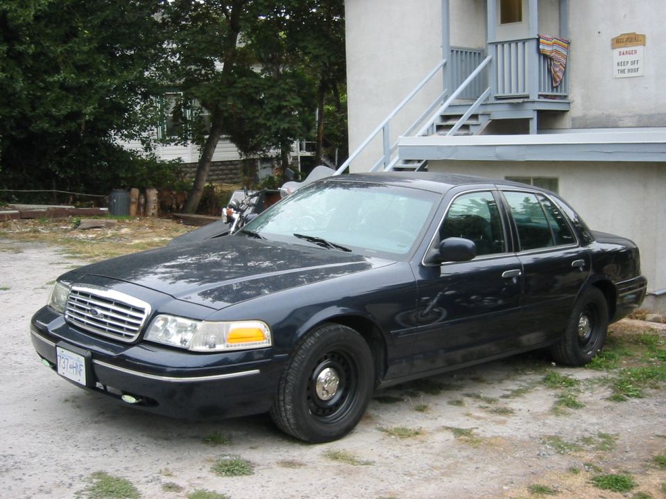 Dark blue sedan parked on dirt, front quarter view. Visible damage on front bumper