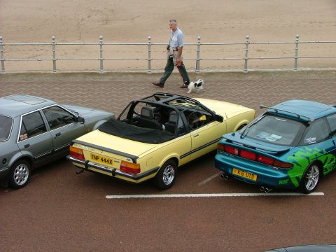 2001 Ford Fiesta - A man walks his dog along a promenade next to three parked cars, including a yellow convertible.