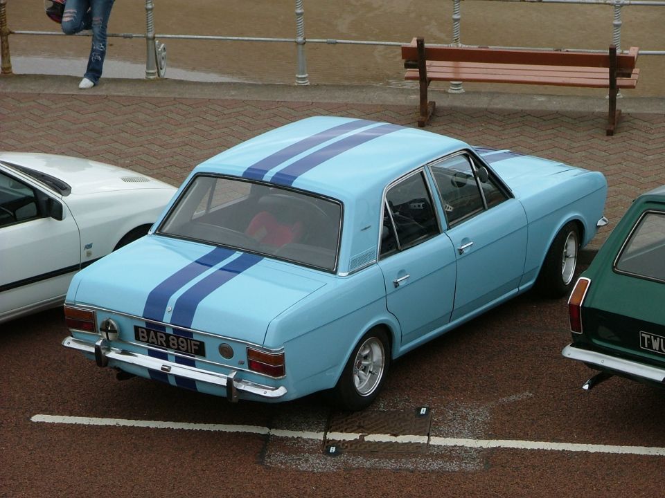 Light blue sedan with dark blue racing stripes, chrome bumper, and license plate BAR 891F parked next to a white car