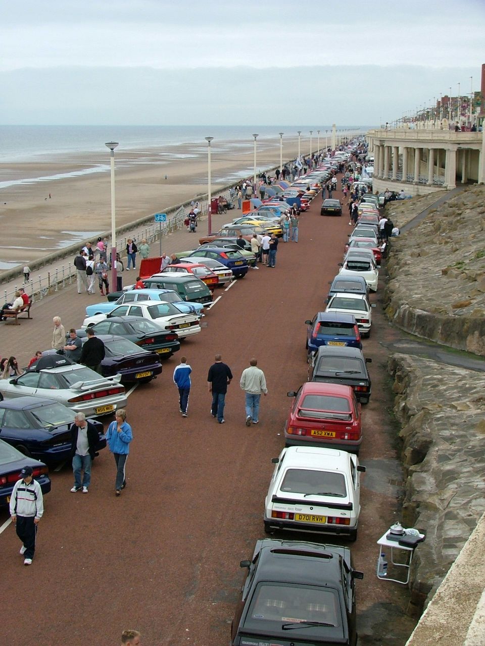 Cars parked along a seaside promenade with people walking by