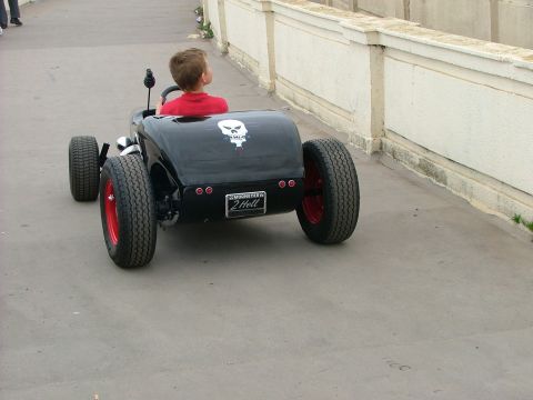 2001 Ford Fiesta - A child drives a black hot rod with a skull decal and custom license plate.