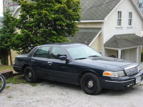 1999 Ford Crown Victoria - A dark blue sedan is parked in front of a house.