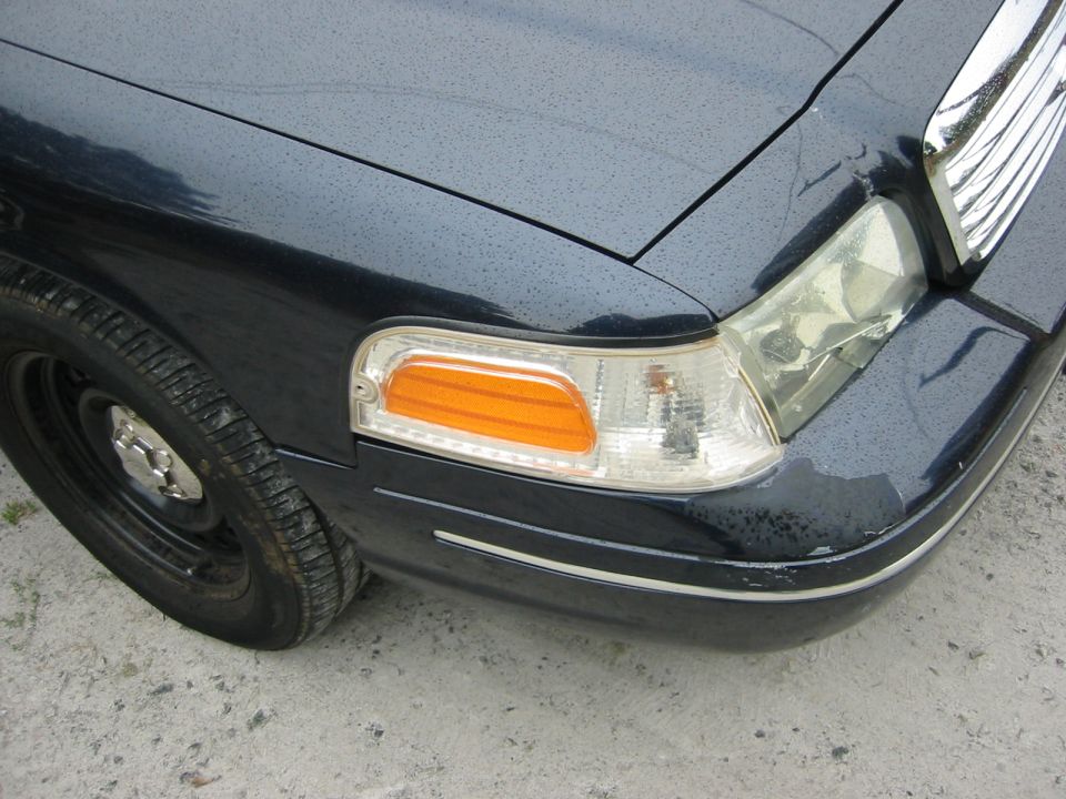 Front corner of dark sedan showing headlight, amber turn signal, chrome trim, and black steel wheel