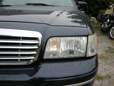 1999 Ford Crown Victoria - Close-up of a dark blue sedan's front end, highlighting the chrome grille and headlight. The grille design suggests a 1998 model year.