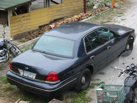 1999 Ford Crown Victoria - A dark blue sedan is parked outdoors next to two motorcycles.