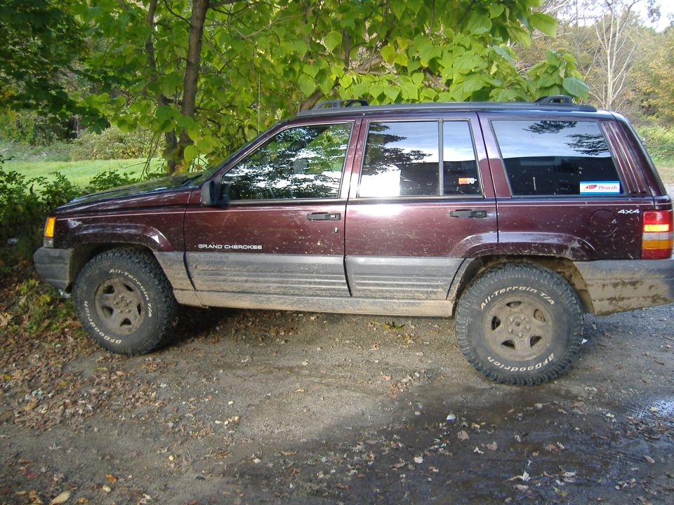 Maroon Jeep Grand Cherokee with off-road tires parked on a dirt road