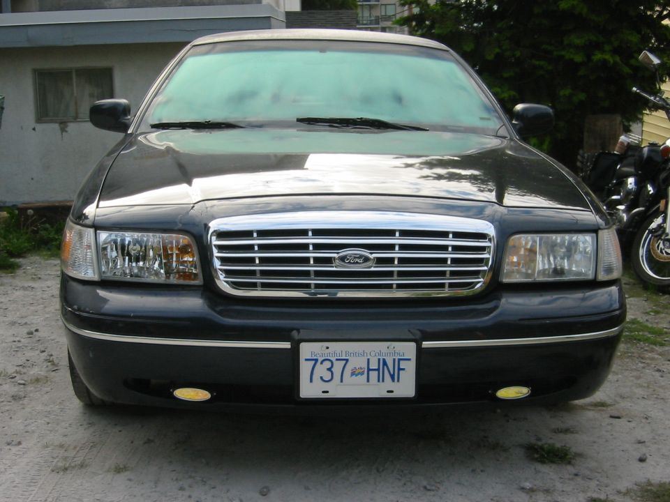 Front view of a black Ford Crown Victoria sedan with BC plate 737 HNF on a gravel driveway