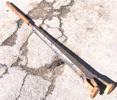 1978 Ford Bronco - A custom-fabricated metal component with a wooden handle lies on a cracked concrete surface.