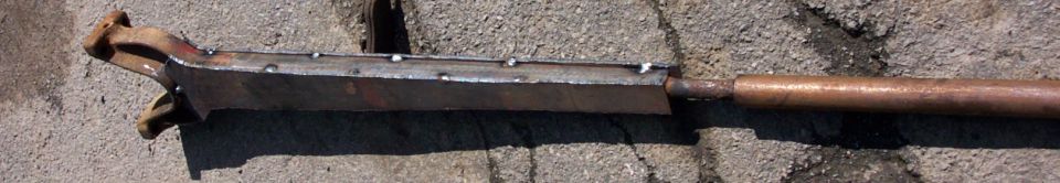 Welded metal tool with a copper pipe handle, resting on concrete