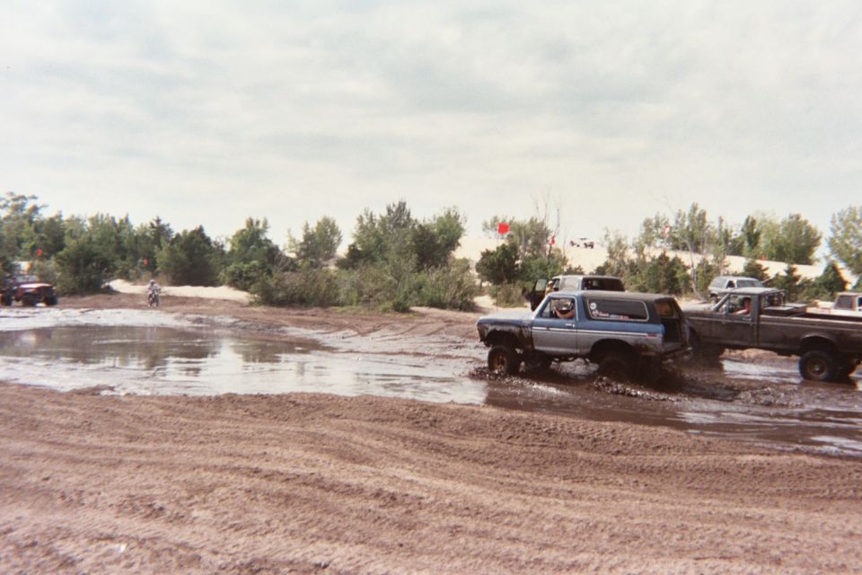 Blue SUV with lifted suspension driving through mud, followed by a dark pickup truck