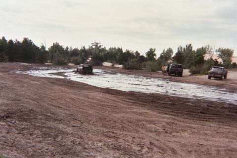1979 Ford Bronco - Off-road vehicles navigate a challenging muddy terrain under a cloudy sky.