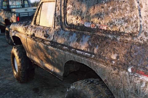 1979 Ford Bronco - This heavily mud-caked 1979 Ford Bronco is seen from the side, with another truck partially visible in the background.