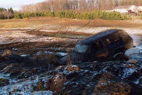 1979 Ford Bronco - A black SUV is stuck in a muddy field with snow scattered around.