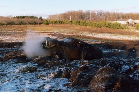 1979 Ford Bronco - A 1979 Ford Bronco is stuck in a muddy, snowy field, emitting steam from its engine compartment.