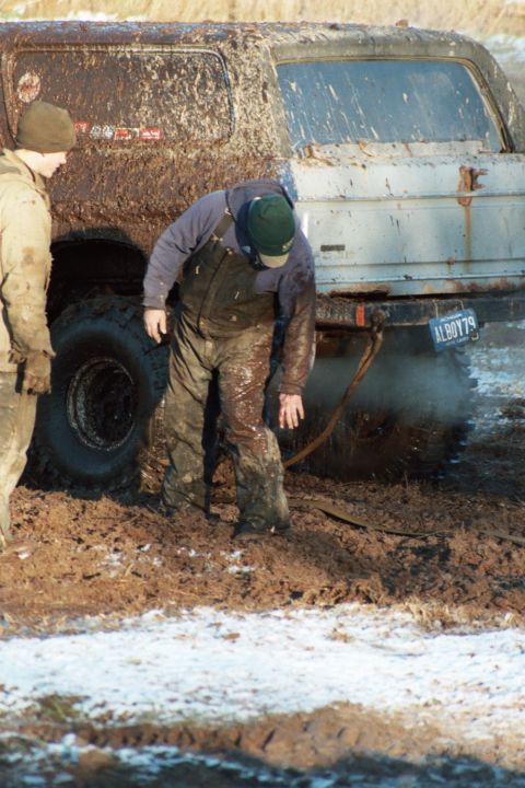 1979 Ford Bronco - A muddy 1979 Ford Bronco is stuck in the mud with two people attending to it.