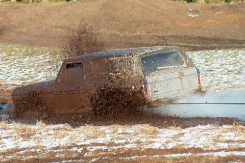 1979 Ford Bronco - Ford Bronco struggles through thick mud, snow on the ground.