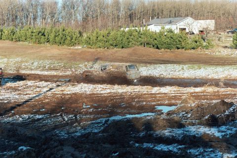 1979 Ford Bronco - A vehicle is stuck in a muddy track with some snow on the ground, while another vehicle is partially visible on the left.