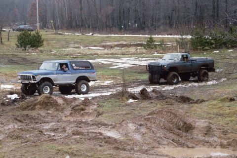 1979 Ford Bronco - A lifted 1978 Ford Bronco navigates a muddy track during a winter event, with another modified pickup truck following closely.