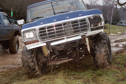 1979 Ford Bronco - This lifted Ford truck is navigating a muddy, off-road course with another vehicle nearby.