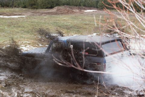 1979 Ford Bronco - Ford Bronco is stuck in the mud, spraying dirt and water as it tries to get out.