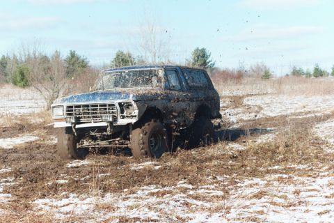 1979 Ford Bronco - A heavily mud-splashed 1978 Ford Bronco navigates a challenging off-road terrain during winter.