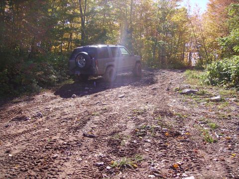 2000 Chevrolet Tahoe - A dark SUV navigates a muddy trail through a wooded area.