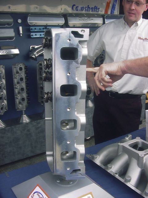 1990 Ford Mustang - Close-up of an aluminum engine cylinder head, likely for a performance application, displayed in a retail or trade show setting.