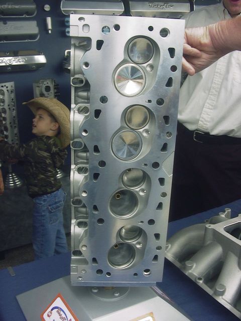 1990 Ford Mustang - A close-up of an aluminum engine cylinder head is displayed, with a young boy observing it.
