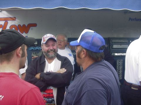 1990 Ford Mustang - Men gathered and talking in front of a trailer with a blue awning overhead.