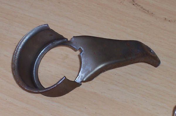 Metal bracket with a circular opening and a bent tab, lying on a wooden surface