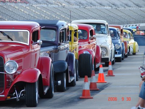 1987 Ford Bronco - A row of classic cars, including a red hot rod, are lined up at an event.