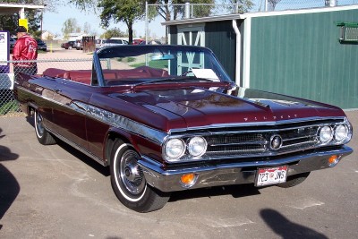 1972 Ford Ranchero - A classic maroon convertible with a black top is parked outdoors near a green building.