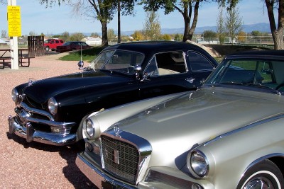 1972 Ford Ranchero - Two classic automobiles are parked together in an outdoor lot, with trees and a distant red vehicle in the background.