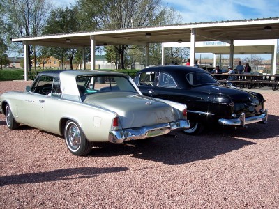 1972 Ford Ranchero - Two vintage cars, a silver coupe and a black sedan, are parked side-by-side under an outdoor pavilion.