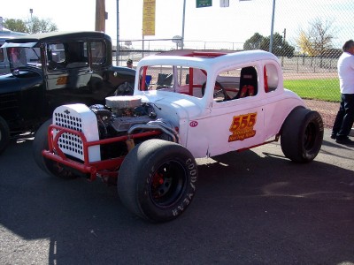 1972 Ford Ranchero - A custom-built coupe race car with a prominent roll cage and racing slicks sits parked next to a vintage truck.