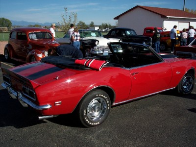 1972 Ford Ranchero - A bright red convertible with racing stripes is parked at an outdoor event with other vehicles and people.
