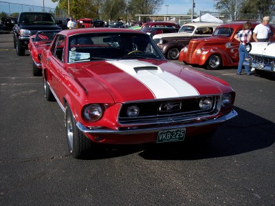 1972 Ford Ranchero - A red 1967 Ford Mustang is parked at an outdoor car show with other vehicles in the background.