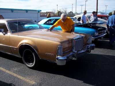 1972 Ford Ranchero - Man cleans a 1977 Lincoln Continental Mark V at a car show with other vehicles present.