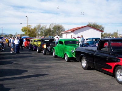 1972 Ford Ranchero - Several custom hot rod cars are lined up in a parking lot on a sunny day.